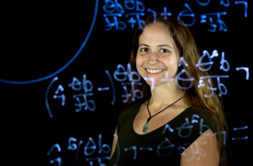 woman standing behind clear glassboard with equations on it