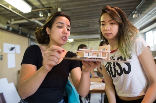 two young women holding a wooden model of a structure