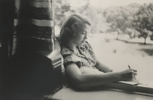 black and white photo of woman doing schoolwork in front of a window