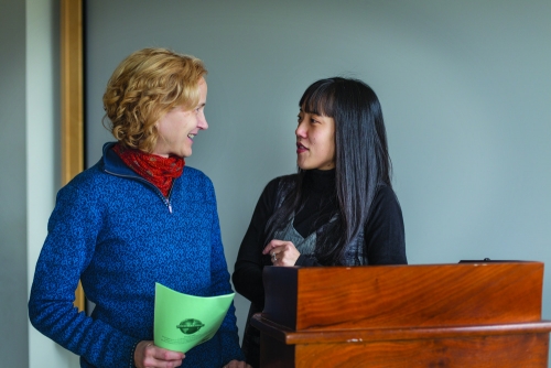 two professors standing at a lectern regard each other with collegiality and warmth