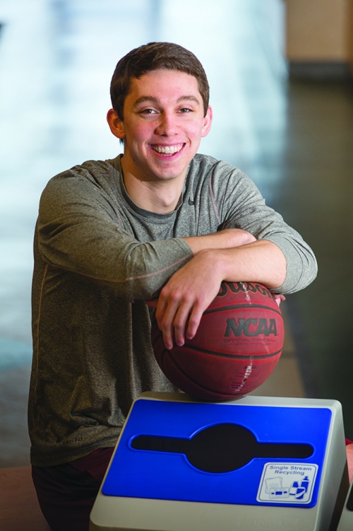 young man leans on a basketball sitting on a recycling bin