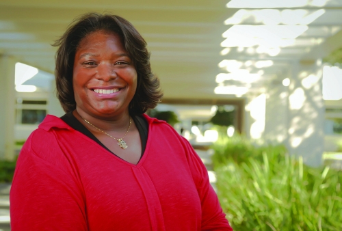 a smiling woman in a red blouse stands in front of ferns