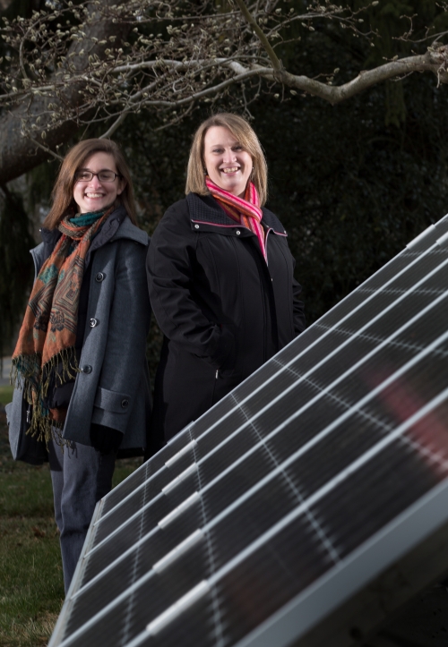 Melissa Tier ’14 and Aurora Winslade stand next to a solar panel.