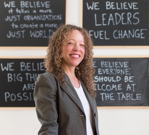 A woman smiles in front of a chalk board 