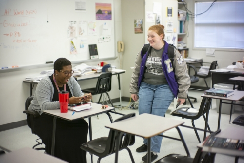 Kimberly St. Julian-Varnon seated in a classroom desk, laughing with a student