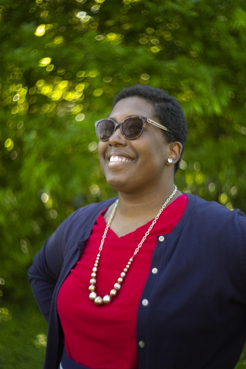 Kimberly St. Julian-Varnon in a red shirt and blue sweater against a backdrop of trees, smiling