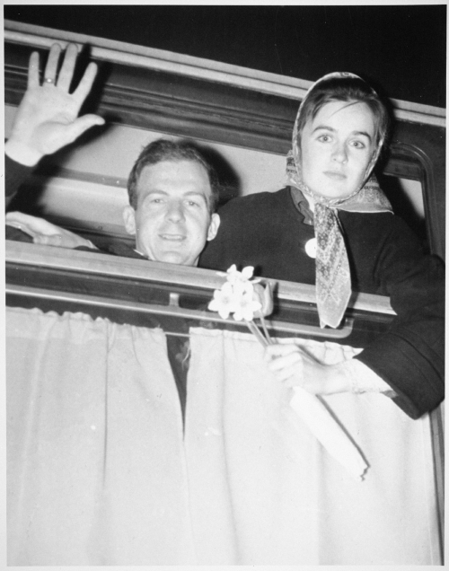 Lee Harvey Oswald waving out a train window, next to wife Marina Oswald