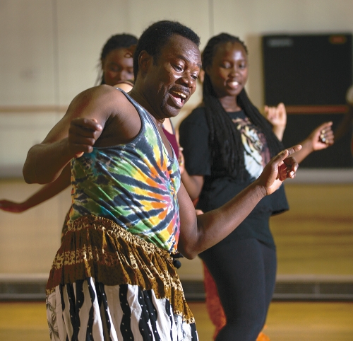 An African American man is dancing in a room with students. 