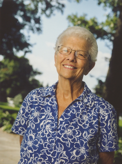 An older woman with glasses smiles at the camera. 