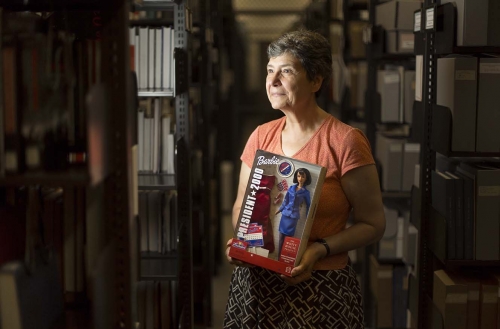 a curator stands in the Peace Collection holding a President Barbie doll box