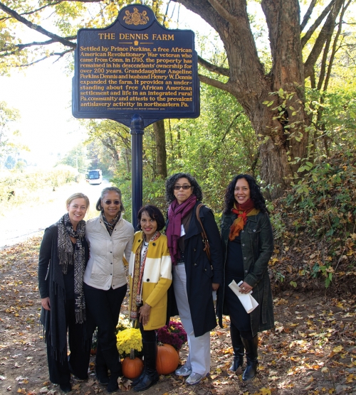 Several women stand outside under a historical marker