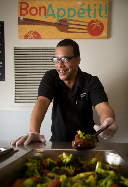 A man stands behind a tray of food. 