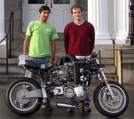 two students stand in front of a motorcycle
