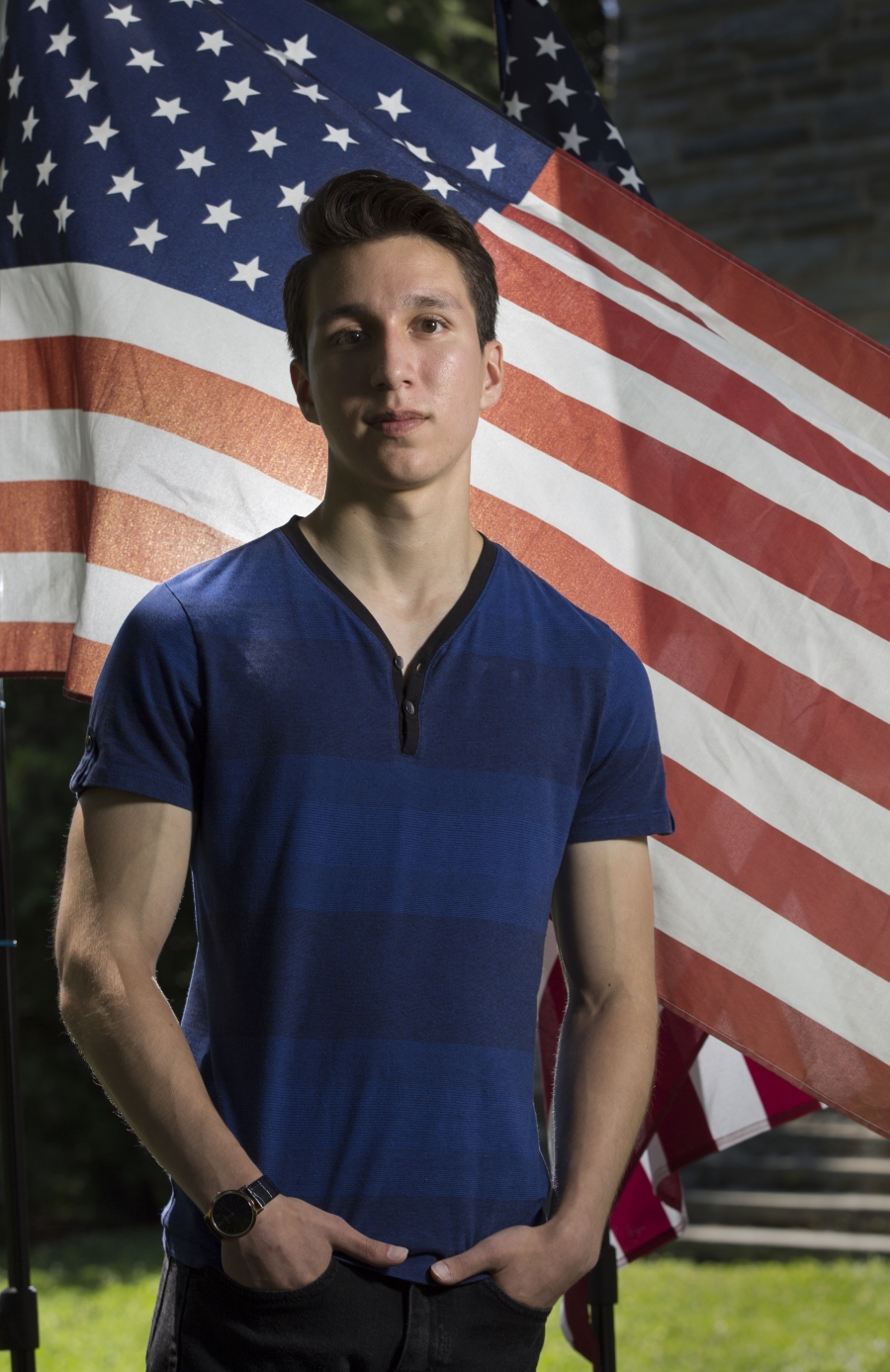 a young man in a blue shirt stands in front of an American flag