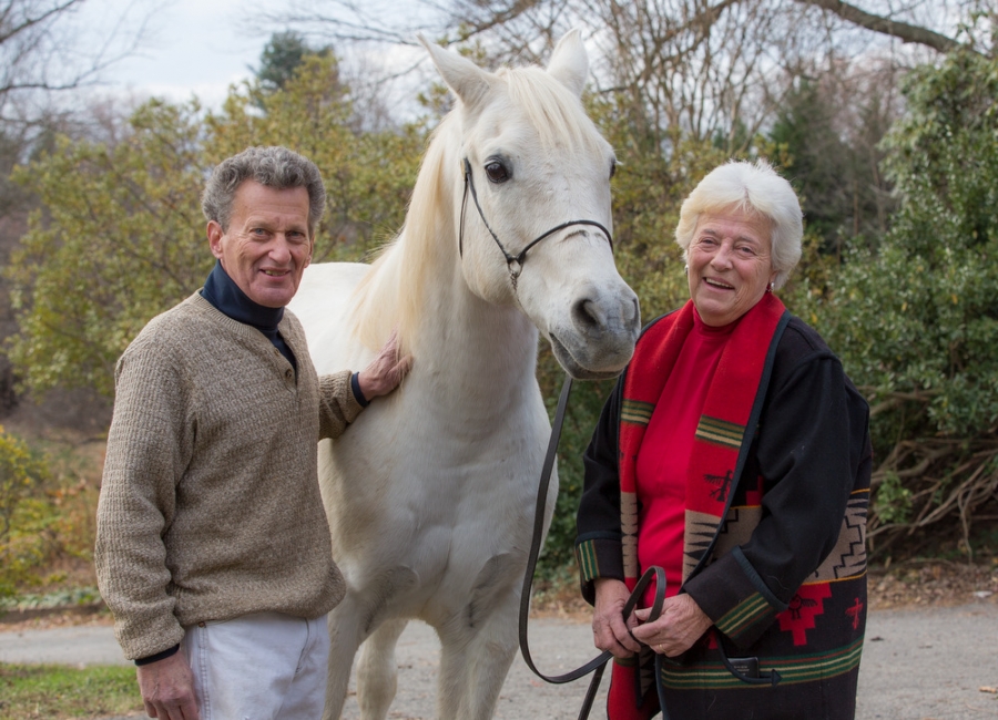 an older couple smile while standing next to a white horse