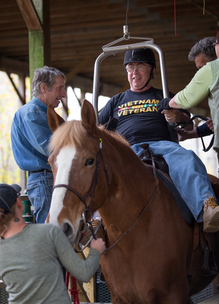 a middle-aged man wearing protective gear rides a brown and white horse