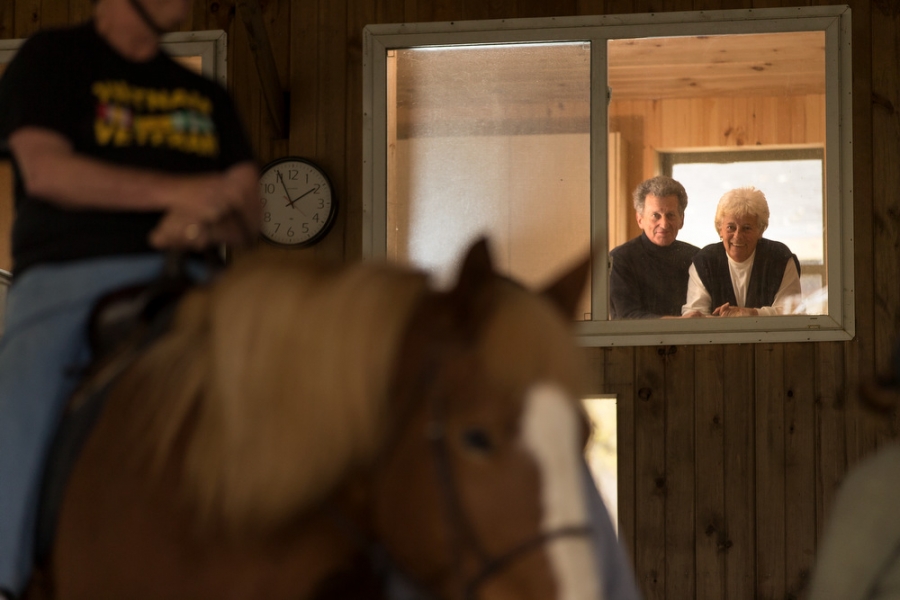 an older couple looks on as horseback riders pass