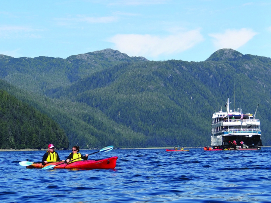 Kayakers on blue water beset by a range of mountains behind them.