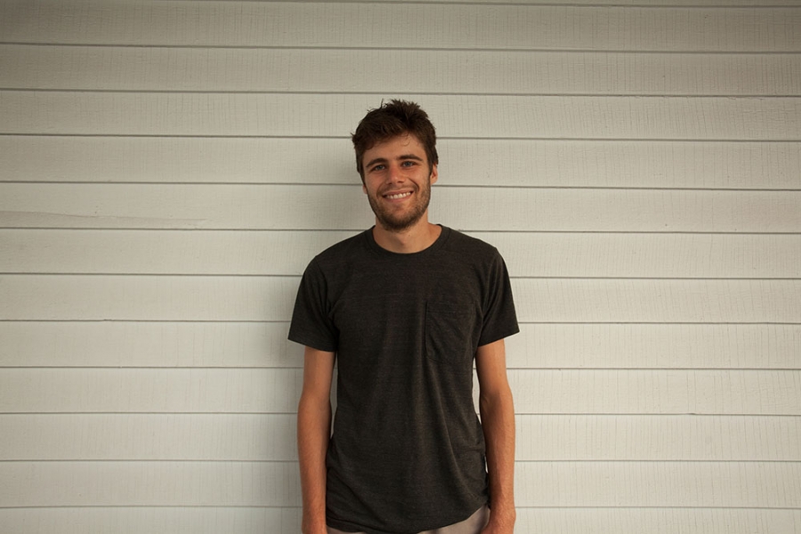 a student stands against a white wall wearing a black shirt