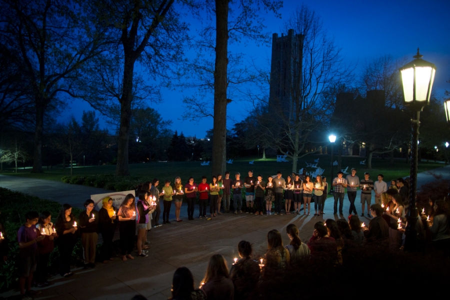 a wide shot of the candlelight vigil with the campus silhouette visible in the back