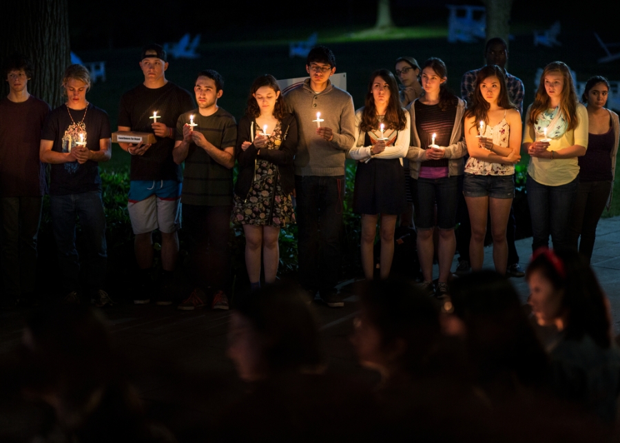 students in darkness lit only by the candles they carry