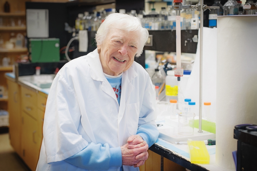 An elderly woman scientist is standing in a lab.