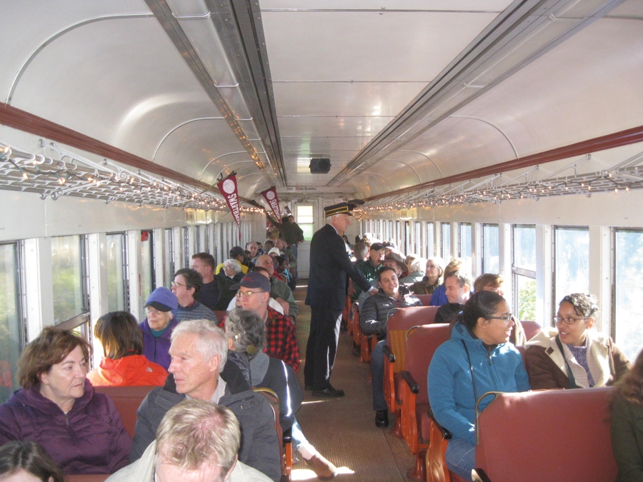 A group of older people are on a train with conductor/professor Frank Moscatelli as a guide.