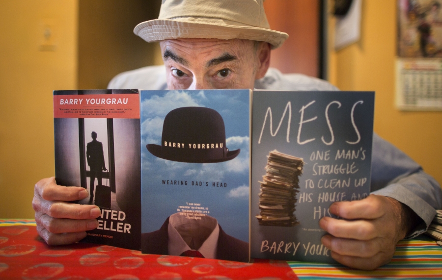 a man in a hat holds up three of the books he's written