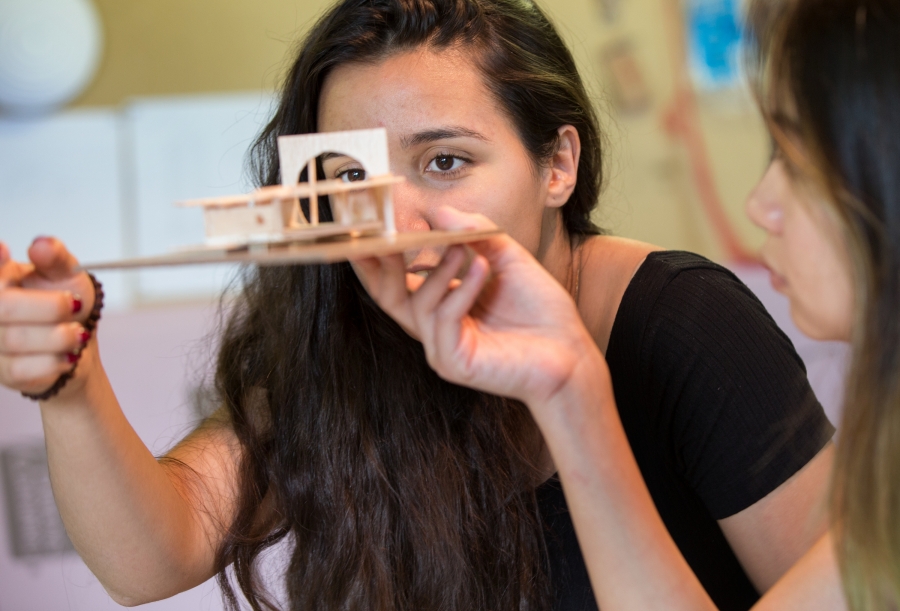 young woman looks up close at a wooden model