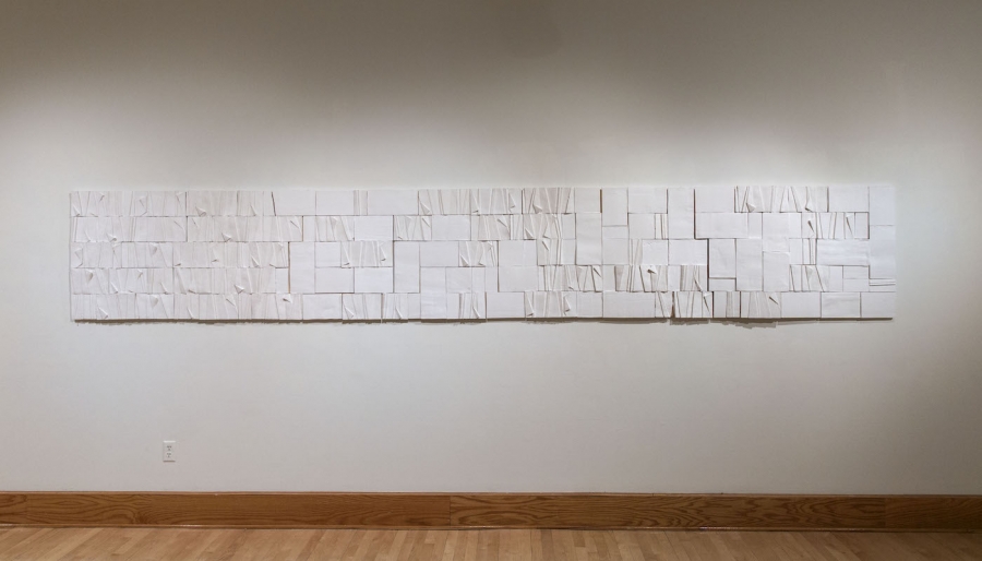 A long, white horizontal art panel of paper cut-outs.