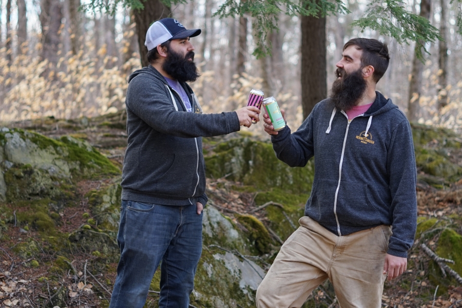 Avery Schwenk and Christophe Gagne in a wooded setting "cheers-ing" cans of Hermit Thrush