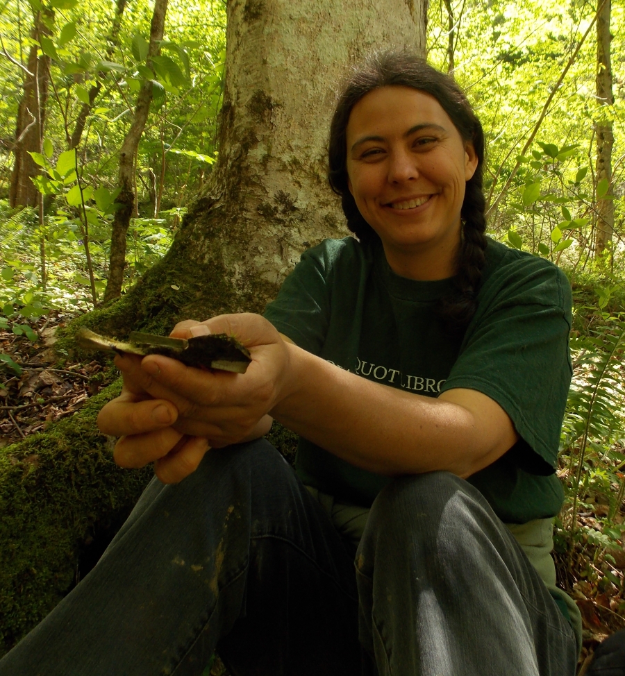 Anna Hess ’00 sitting by a tree in the forest