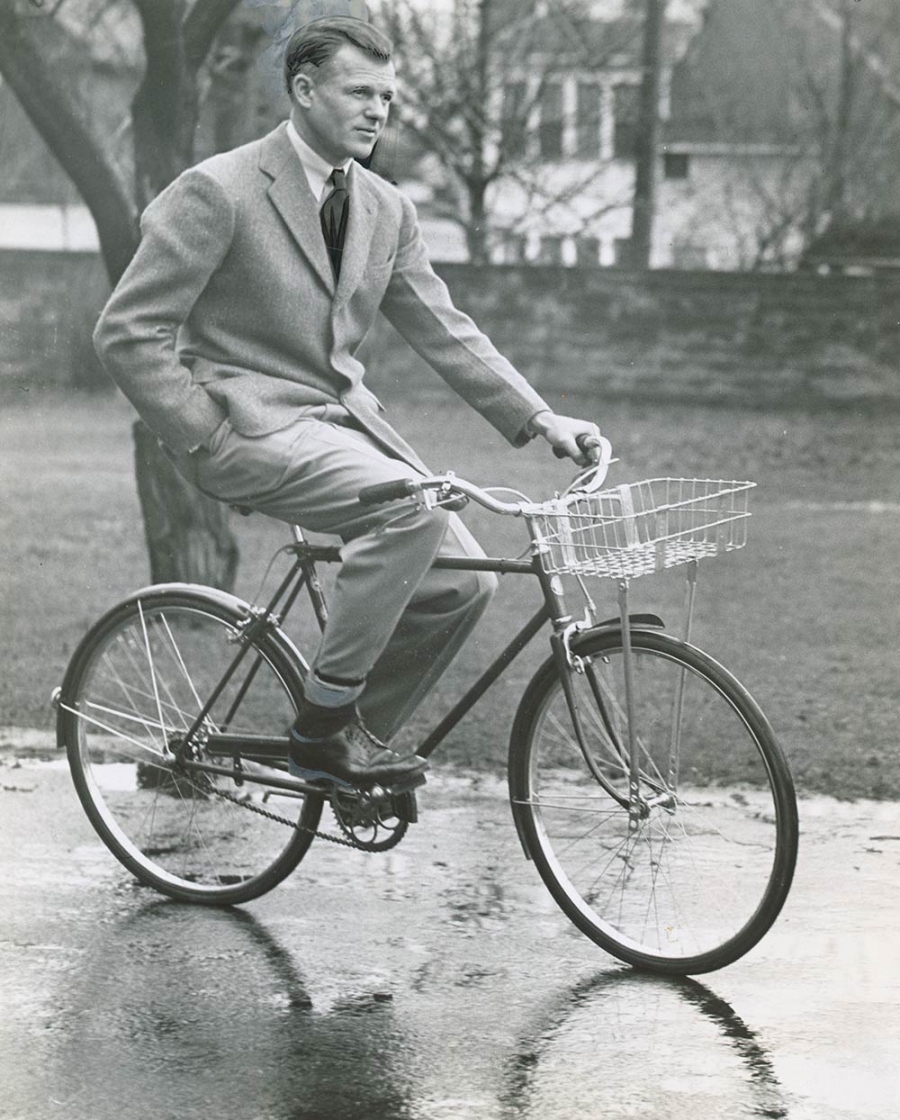 black and white photo of man in suit and tie riding a bicycle