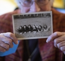 Barbara Lea Couphos holding a B&W photo of six women