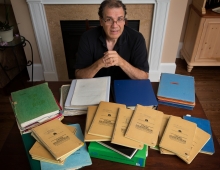 Matt Zencey ’79 sits in a well furnished home in front of a fireplace with his college notebooks scattered before him.