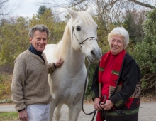 an older couple smile while standing next to a white horse