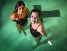 two women stand in the green water of a swimming pool