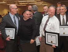 A group of middle-aged men hold plaques and smile.