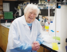 An elderly woman scientist is standing in a lab.