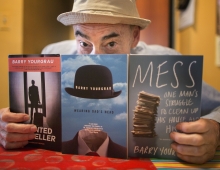 a man in a hat holds up three of the books he's written