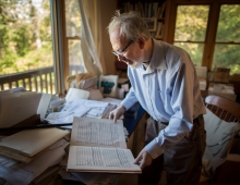 A man is standing in a room looking at a book. 