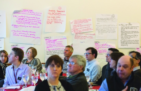 community members sit in a room underneath handwritten signs, listening