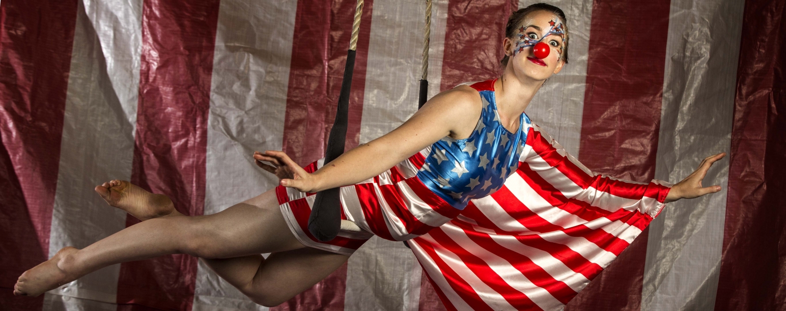 Joanna Wright '08 on a trapeze, dressed in a U.S. flag costume and a clown nose