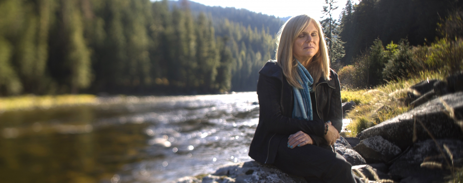 portrait of Anna Peterson ’83 sitting on a rock by a river
