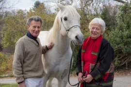 an older couple smile while standing next to a white horse