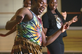 An African American man is dancing in a room with students. 
