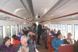 A group of older people are on a train with conductor/professor Frank Moscatelli as a guide.