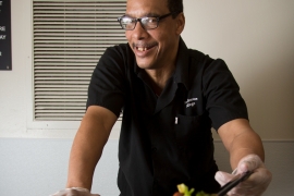 A man stands behind a tray of food. 