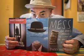 a man in a hat holds up three of the books he's written