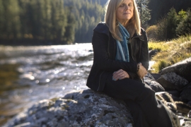 portrait of Anna Peterson ’83 sitting on a rock by a river